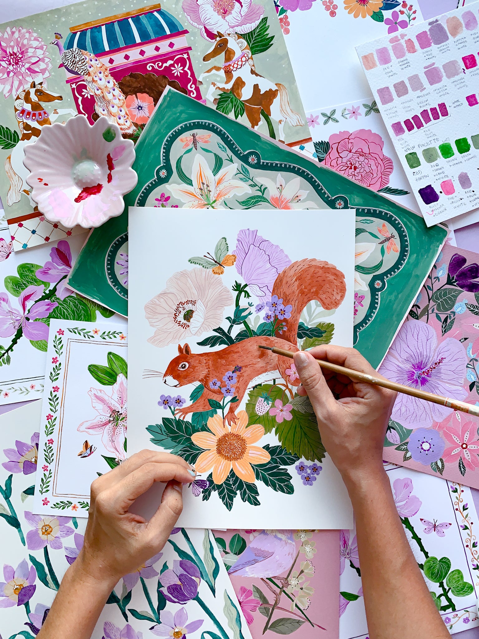 Person painting a squirrel among flowers on a colorful art project with design swatches.
