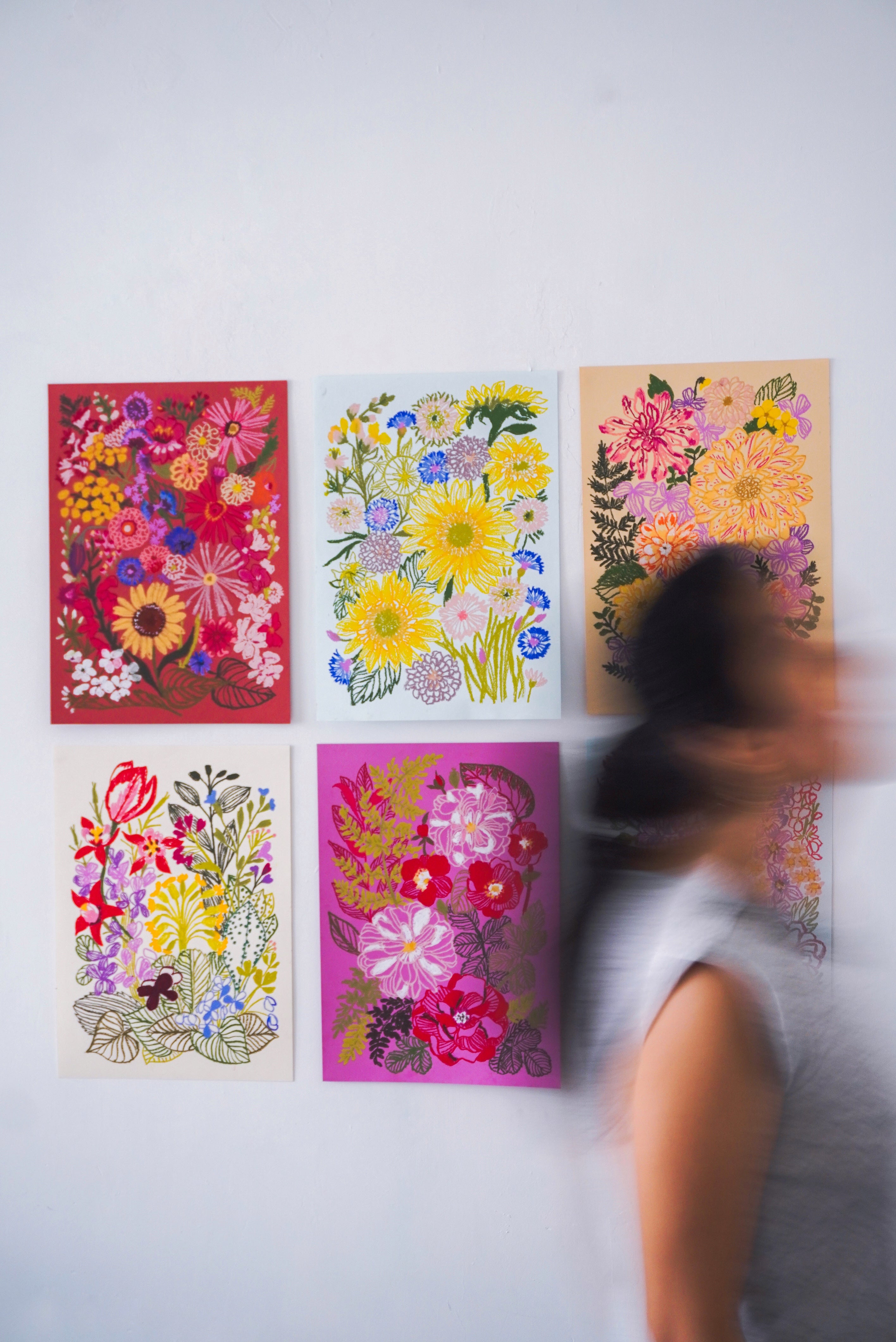 Person standing in front of six colorful floral paintings on a white wall